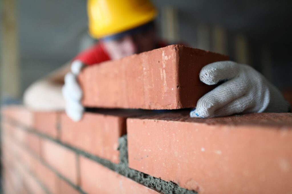 close-up-professional-construction-worker-laying-bricks-industrial-site-builder-protective-uniform-man-building-wall-with-blocks-renovation-concept